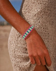 MyAleph Riviera Bracelet in Saint Tropez — emerald green and hot pink evil eye protective charm bracelet worn on wrist, styled with a cream knit summer dress on the beach.
