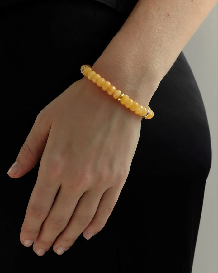 Tangerine quartz beaded bracelet with gold accents worn on wrist, vibrant orange gemstone jewelry styled with black outfit