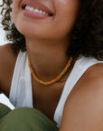 A smiling model wearing the Zoe necklace in tangerine quartz, adding a bright, sunny pop of color to her outfit.