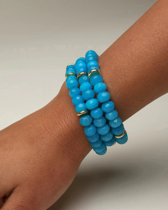 Close-up of the Zoe bracelet stack in vibrant azure blue, worn on a wrist, with smooth beads and subtle gold accents.