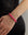A close-up of a person's wrist wearing a beaded stretch bracelet made of bright pink faceted beads separated by small gold spacer rings, paired with a black top.