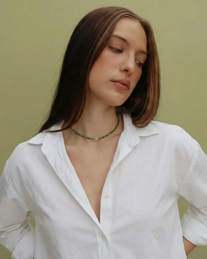 Woman wearing a white shirt with a green evil eye juliana malachite necklace against a green background